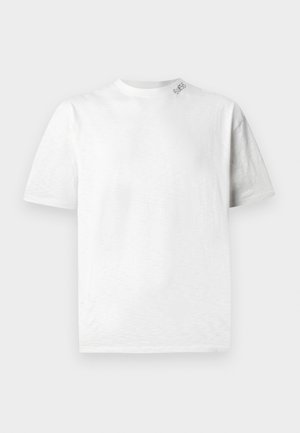 Camiseta blanca de manga corta con cuello redondo, que presenta una textura sutil y un pequeño logotipo en el hombro izquierdo.