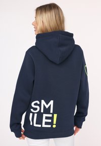 Marineblaues Hoodie aus Baumwolle mit einer Vordertasche, auf der Rückseite mit dem Schriftzug "SMILE!" in Weiß und Neon-Grün bedruckt und mit einer Kordelzugkapuze.