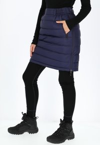 Marine blauwe puffer rok met horizontale quilting; beschikt over een zijzak met rits en een elastische tailleband. Gecombineerd met zwarte legging en laarzen.