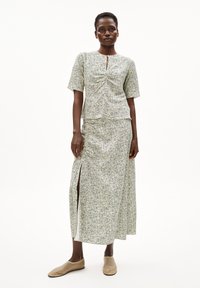 Blumengemusterter Zweiteiler in gedecktem Grün und Weiß, bestehend aus einem gerafften Oberteil und einem langen, geschlitzten Rock, kombiniert mit beigen Slippers.