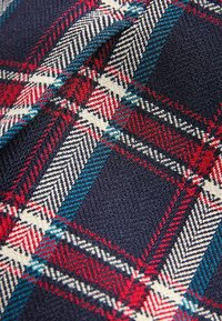 Gewebter Stoff mit navy-blauem Grund, der ein Karomuster in Rot, Weiß und Teal aufweist, mit strukturierter Oberfläche und feinen Details.