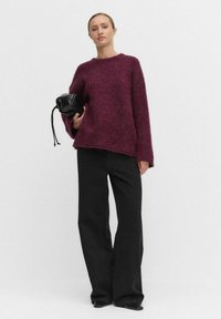 Vinröd, fluffig stickad tröja med rund halsringning och sidoklipp, tillsammans med svarta byxor med vida ben som har ett subtilt prickigt mönster.