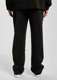 Sorte fløjl bukser med et bredt ben-design, der har subtile lodrette ribben og en afslappet pasform. Sammen med hvide sneakers.