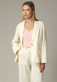 Lichtromkleurig linnen blazer met een enkele knoop, geknipt revers en een linkse zak, gecombineerd met een zachtroze V-hals top.