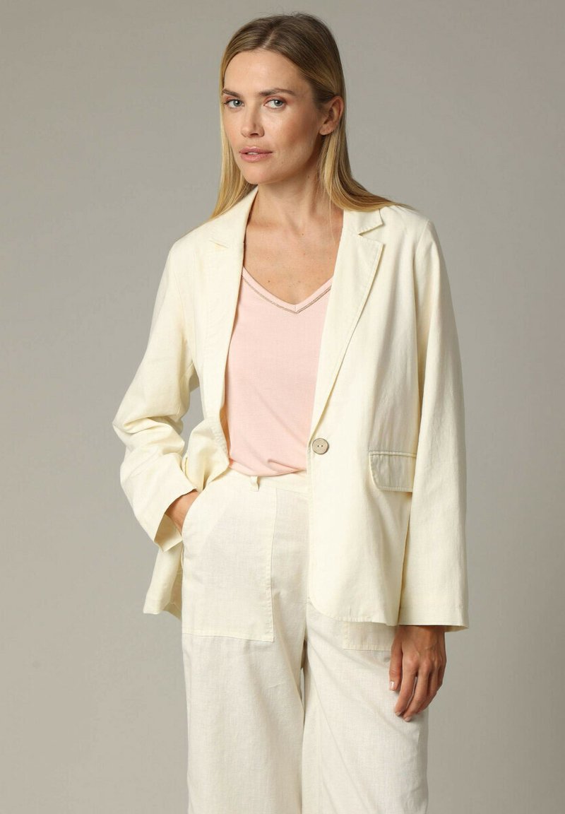 Lichtromkleurig linnen blazer met een enkele knoop, geknipt revers en een linkse zak, gecombineerd met een zachtroze V-hals top.