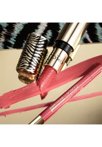 Gold lipstick with zebra print cap and pink lip liner laying on a reflective surface with pink lipstick and liner swatches.