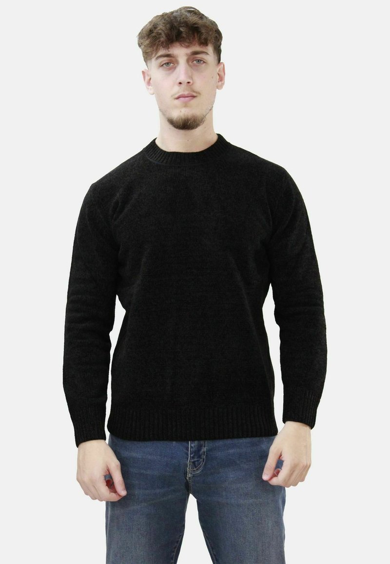 Maglione nero a maglia con scollatura rotonda e polsini e orlo a coste. Indossato con jeans blu, che mostrano una silhouette aderente e un tessuto texture.