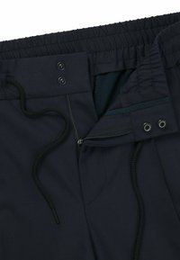 Navy blue pants with an elastic waistband, adjustable drawstring, zipper closure, and dual snap buttons. Smooth fabric with visible seams.