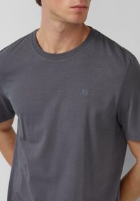 Grijze katoenen t-shirt met een ronde hals, korte mouwen en een subtiele logo op de linkerborst. Zachte textuur en casual pasvorm.