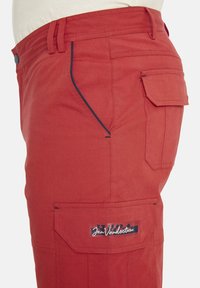Rote Cargo-Hosen mit mehreren Taschen, die kontrastierende blaue Paspelierung entlang der Seitennähte und ein Markenlabel auf der Gesäßtasche aufweisen.