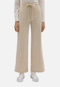 Pantalones de chándal de pierna ancha en color beige, hechos de tejido suave, con cintura ajustable y un corte relajado, combinados con zapatillas blancas.