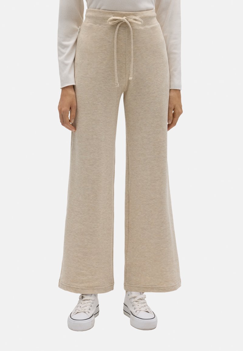 Pantalones de chándal de pierna ancha en color beige, hechos de tejido suave, con cintura ajustable y un corte relajado, combinados con zapatillas blancas.