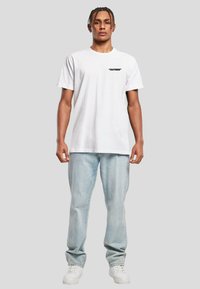 Hvit bomull T-skjorte med korte ermer, med svart "OUTSIDE" tekst på brystet. Kombinert med lyseblå jeans og hvite joggesko.