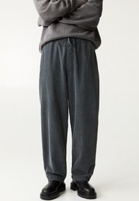 Grijze corduroy broek met een relaxte pasvorm, voorzien van een elastische tailleband en een trekkoord, gecombineerd met zwarte chunky laarzen.