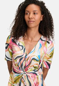 Wielokolorowa sukienka w stylu wrap, wykonana z lekkiego materiału, z głębokim dekoltem w kształcie V, krótkimi rękawami oraz wiązaniem w talii.