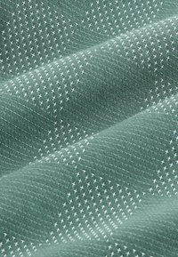 Gros plan sur un tissu vert avec des motifs de points de croix blancs texturés disposés en rangées diagonales sur la surface.