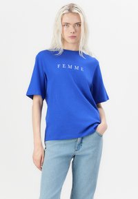 Blauwe crewneck t-shirt met het woord "FEMME" in het wit gedrukt. Korte mouwen, relaxte pasvorm, gemaakt van zachte cotton stof.