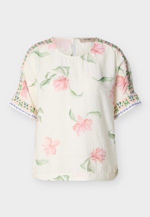 Blouse courte à manches courtes crème avec imprimé floral rose et feuilles vertes, ornée de motifs décoratifs en bordure verte et bleue sur les manches.