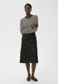 Gestreifter schwarz-weißer Cardigan mit Knöpfen, kombiniert mit einem langen schwarzen Lederrock und schwarzen Ballerinas. Glatte Textur, klassischer Stil.