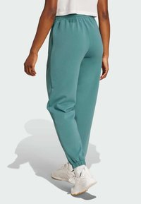 Teal Jogginghosen aus weichem Material mit elastischem Bund, Seitentaschen und schmal zulaufenden Bündchen. Getragen mit weißen Sportschuhen.