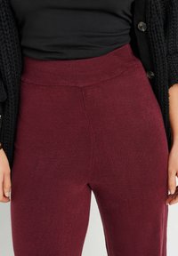 Vinröda tights med ribbad midja och mjuk textur, ihop med en svart stickad cardigan. Närbild på midjan och tyget.