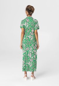 Groene maxi-jurk met bloemenmotief en korte mouwen, voorzien van een wit bloemenpatroon, een aansluitende taille en een uitlopende rok. Inclusief witte sandaaltjes met bandjes.