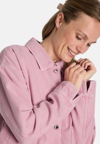 Rosa Jeansjacke mit Kragen, Knopfverschluss und leicht gesenkten Schultern. Der Stoff hat eine weiche Textur und sichtbare Nähte.