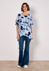 Lightweight, semi-sheer top with a blue and navy circular pattern; features a round neckline and flowing, short sleeves. Paired with flared blue jeans.