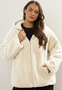 Krämfärgad, plyschig zip-up hoodie med en stor huva, två sidofickor och vida ärmar, tillverkad av mjukt, strukturerat tyg.