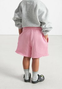 Roze katoenen korte broek met een losse pasvorm en elastische tailleband, gecombineerd met grijze gestreepte sokken en zwarte klompen. Fuzzy oversized grijze sweatshirt.