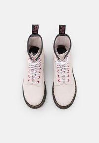 White suede ankle boots with black accents, white and red laces, yellow stitching, and a pull tab at the back.