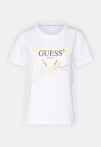 Camiseta de algodón blanca con un logo de triángulo amarillo que dice "GUESS U.S.A." en negro y acentos decorativos en dorado en estilo cursiva.