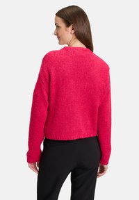 Tassig, avkortad tröja i stark rosa, med en texturerad stickad design och långa ärmar. Bakvy visar en avslappnad passform och rundad halsringning.