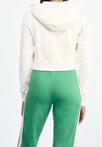 Felpa crema cropped con cappuccio, abbinata a pantaloni jogger verdi con strisce laterali. Il tessuto morbido e il design aderente migliorano il comfort.