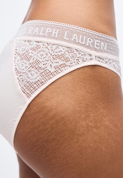 Κοντινό πλάνο ενός ατόμου που φοράει ανοιχτό ροζ δαντελένια εσώρουχα με λουλουδάτο μοτίβο και εμφανή ζώνη μέσης "Ralph Lauren".