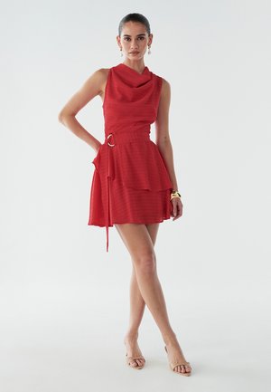 Vestido rojo sin mangas con escote drapeado, falda con volantes en capas, detalle de lazo lateral y hebilla de cinturón circular. Tejido suave y texturizado.
