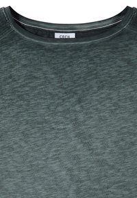 Haut en tissu texturé vert avec un col rond et une petite étiquette blanche indiquant le nom de la marque "CECIL" à l'intérieur du col.