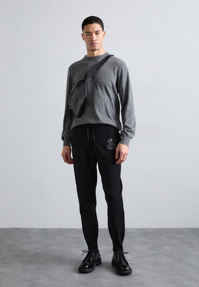 Grauer Pullover mit langen Ärmeln, schwarze Jogginghose mit einem Aufnäher, schwarze Umhängetasche und schwarze Schnürschuhe. Schlichtes und modernes Design.