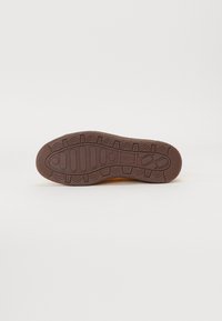 Semelle de chaussure en caoutchouc marron avec un motif de bande de roulement texturé, comprenant des grips en zigzag et circulaires pour la traction, conçue pour la durabilité et une utilisation en extérieur.