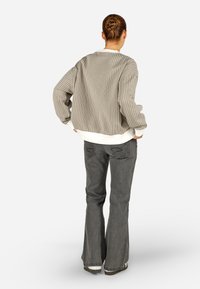 Csíkos, oversized világosszürke zakó fehér mandzsettákkal, sötétszürke harangszárú nadrággal párosítva, amelynek hátsó zsebének varrási részlete van.