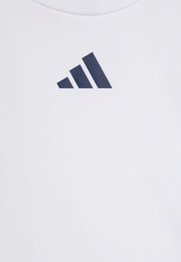 Camiseta atlética blanca con un gráfico del logo de Adidas en azul marino y tres franjas diagonales. El material parece suave y ajustado.