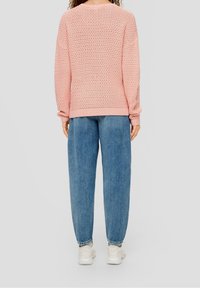 Pull en tricot rose à coupe ample, motif texturé, encolure ronde et poignets côtelés, associé à un jean large bleu et des baskets blanches.