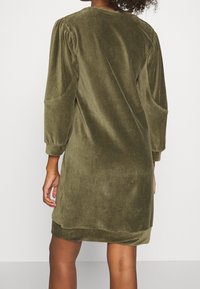 Vestido de terciopelo verde oliva con mangas largas abullonadas, cuello redondo y aberturas laterales. Textura suave y corte relajado.