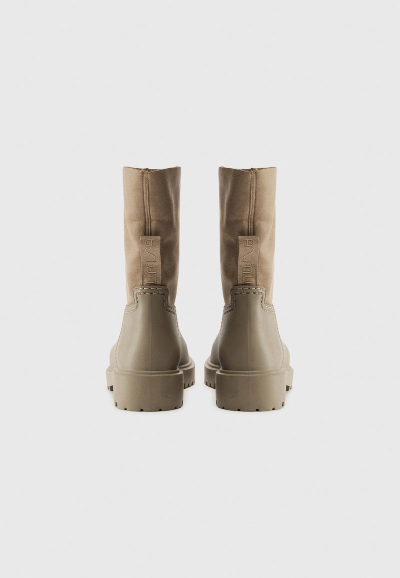 Botas de tobillo de tela marrón con una parte superior texturizada en tono marrón claro y suelas de goma. Presentan un logo de la marca en relieve en la parte posterior y una silueta elegante.