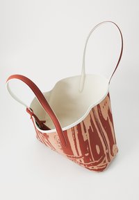 Red and beige tote bag with a textured pattern. Features two long handles and a contrasting white interior. Open, spacious design.