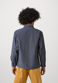 Navy blue, lightweight cotton shirt with long sleeves, button cuffs, and a collared neckline, featuring a smooth texture and straight hem.