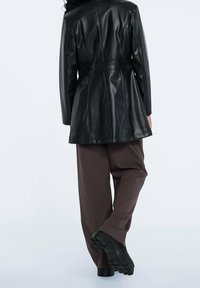 Chaqueta de cuero negra con cintura ajustada y dobladillo acampanado, combinada con pantalones marrones holgados y calzado negro con textura.