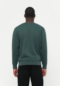 Donkergroen katoenen sweatshirt met lange mouwen, geribbelde manchetten en zoom, met een ronde halslijn en een gladde textuur.