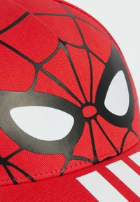 Gorra roja con un patrón de telaraña, que presenta grandes formas de ojos blancos con contornos negros. Incluye tres franjas blancas en el borde.