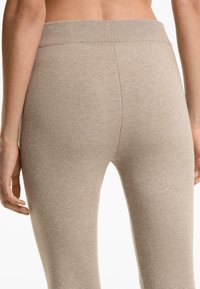 Close-up van de onderrug en heupen van een persoon die hooggekraagde, beige gebreide broeken draagt met een geribbelde tailleband.